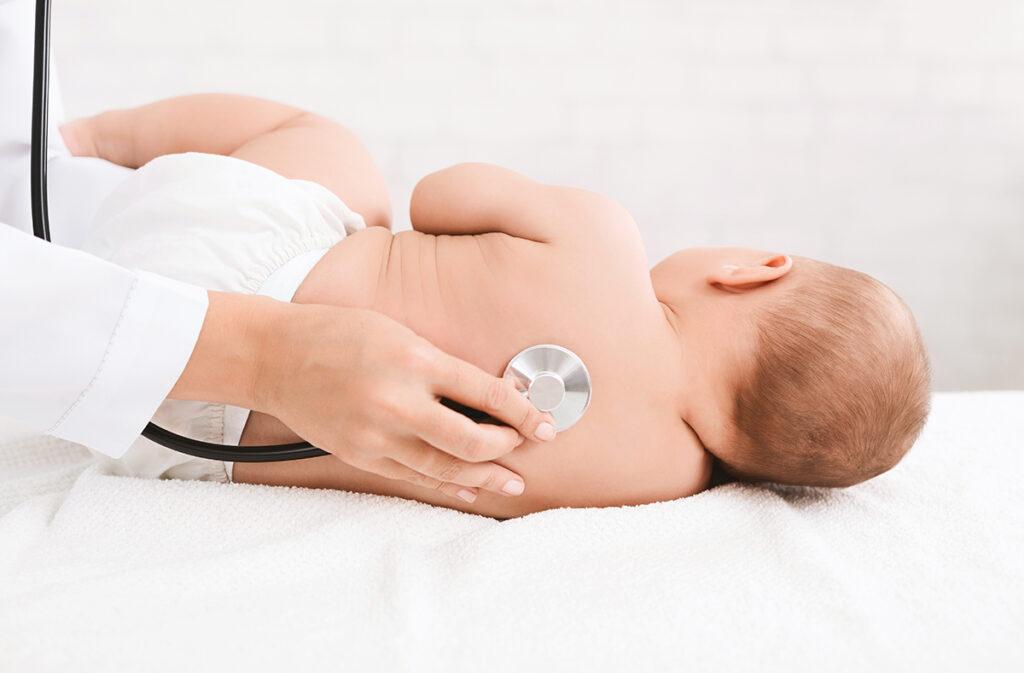 Children's doctor exams baby with stethoscope, listening his back in hospital